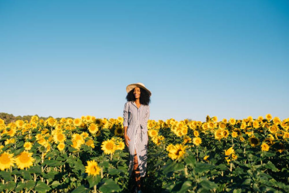A woman walks through a field of blooming sunflowers on a bluebird sky day, she seems to exude the essence of the importance of self-love.