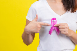 Woman holds breast cancer pink ribbon, pointing at it to encourage others to understand mammogram screening guidelines.