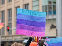 People gather at a bi visibility awareness month march, one protestor holds a sign with the bisexual flag colors that reads 