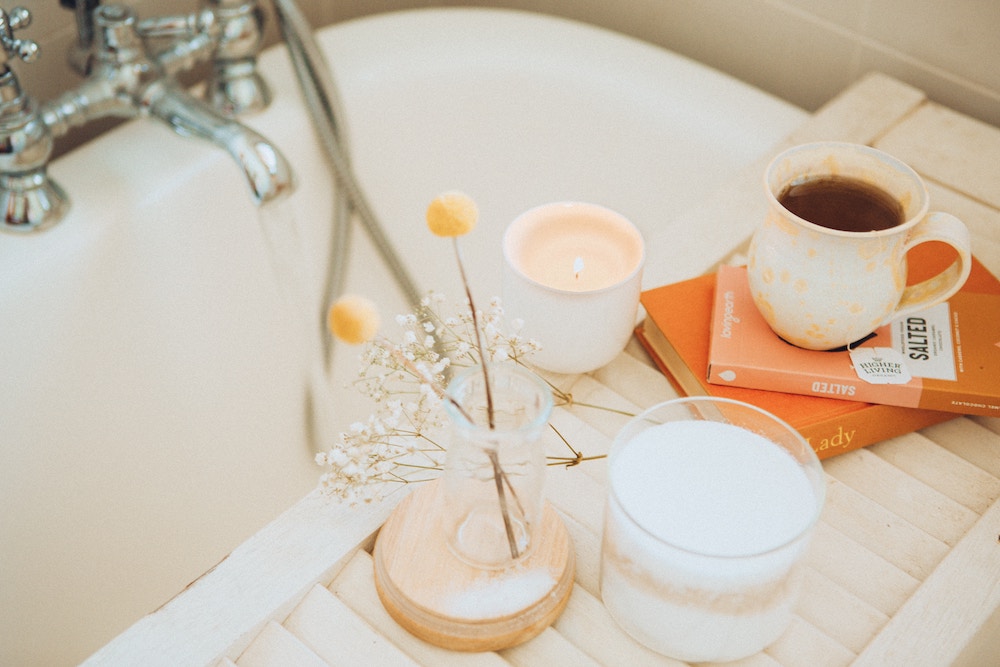 When considering how to give back to the community, it's crucial to take care of yourself first, like the person in this image is doing with a bubble bath and a cup of tea.