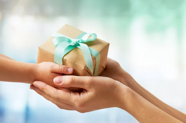 small brown box with blue bow wrapped around it being handed to someone.