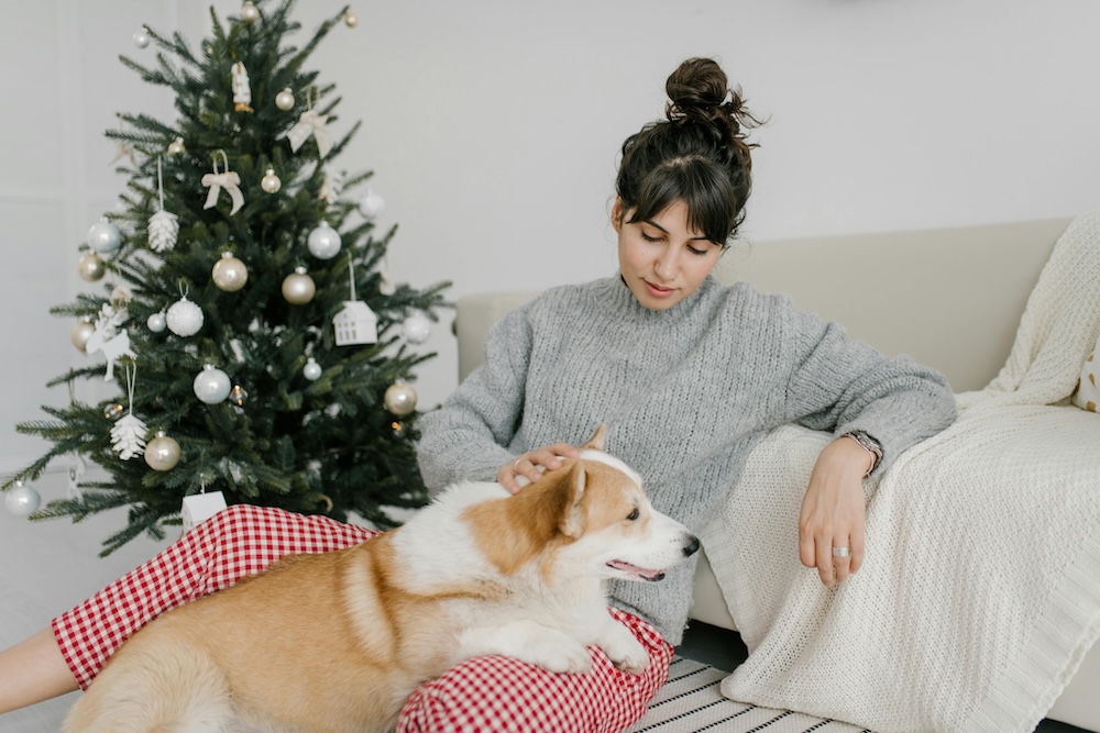 Cozy scene of a woman relaxing by a beautifully decorated Christmas tree with her dog, enjoying self-care and holiday warmth. Perfect holiday vibes with festive decor and pet companionship.