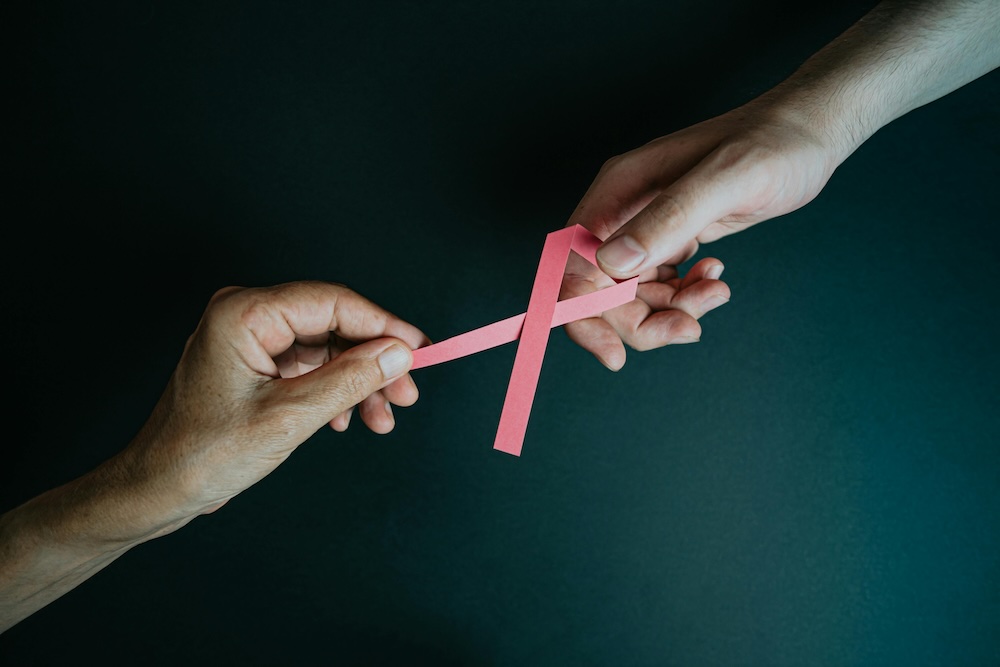 Two hands holding a breast cancer ribbon raising awareness and support.