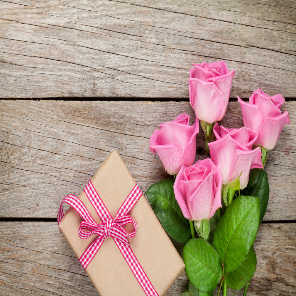 A thoughtful arrangement of pink roses beside a matching gift box on a rustic wooden background, symbolizing the impact of employer matching gift programs for breast cancer support.